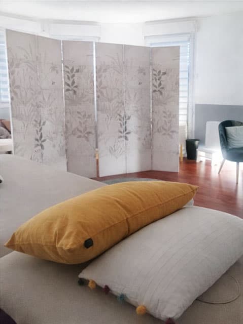 Salle de massage lumineuse du cabinet Blowball à Guyancourt, avec table en bois, coussins colorés et décoration zen pour soins bien-être.